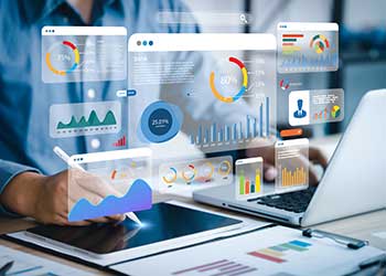 Student or professional reviews interactive data analytics dashboards displayed on transparent digital screens above a laptop and tablet, featuring charts, graphs, performance metrics, and data visualizations that represent business intelligence, statistics, and data science.
