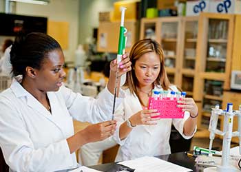 Students perform hands-on chemistry experiments in a laboratory, using pipettes and test tubes to measure and transfer liquids. Working at a lab bench with scientific equipment and materials, students apply practical research and analytical techniques.