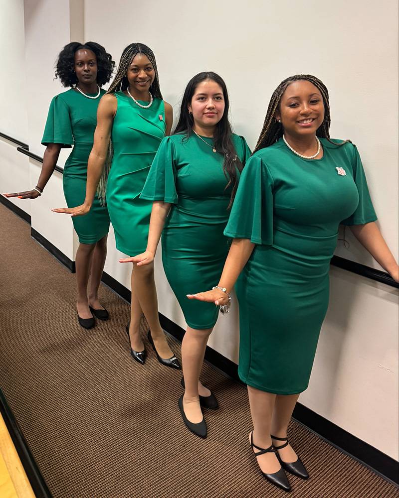 Sigma Sigma Chapter group - four members standing in green dresses, in a line next to a rail