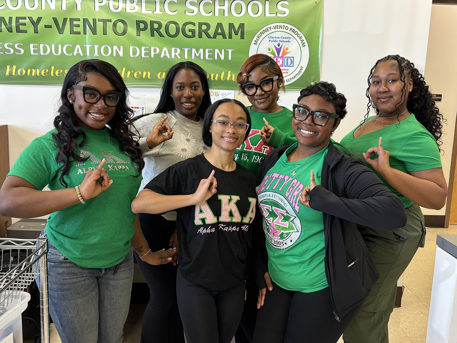 AKA group picture of sixmembers, wearing different variations of AKA t-shirts at a volunteer opportunity for Clayton County Public Schools
