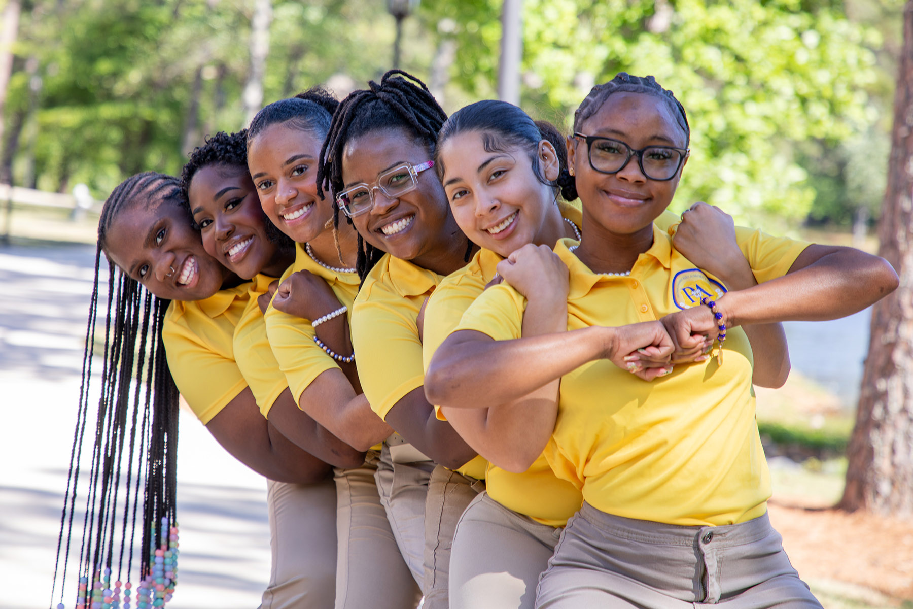 Image of members of the Rho Lambda Chapter of Sigma Gamma Rho in a line, embracing the member in line ahead of them wearing gold shirts with their chapter seal on them.